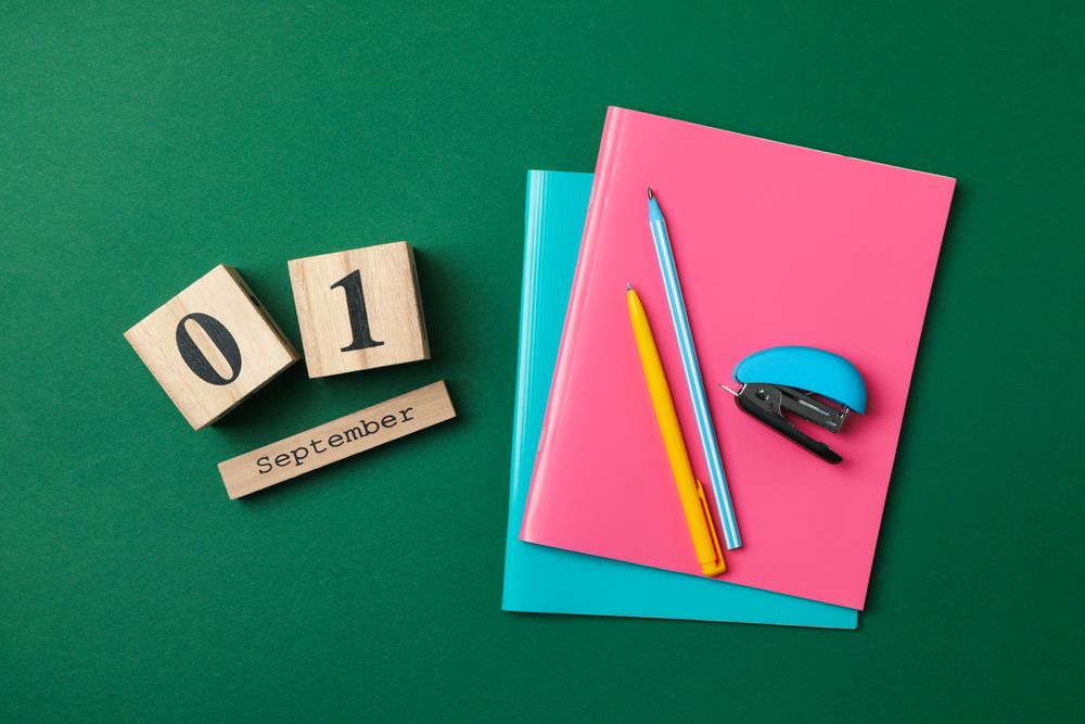 Wooden calendar with 1 september and school supplies on green background