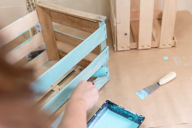 Woman paining wooden box in blue color with roller