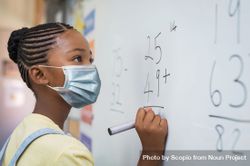 Teenage girl with facemask solving math problem on light board 4NJJg4