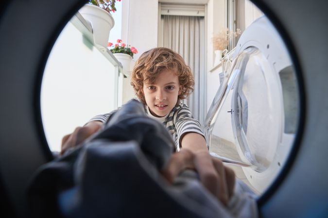 Positive kid taking clothes out of washing machine