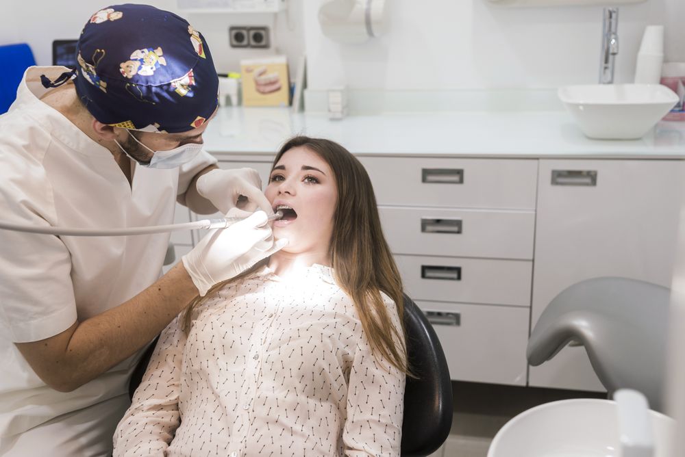 Male dentist drilling tooth in female patient