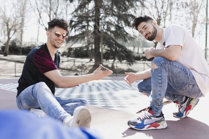 Handsome positive men using smartphone and sitting on floor in park