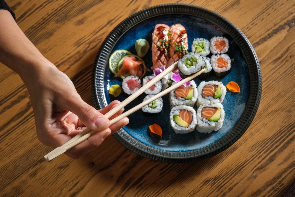 Person taking sushi with chopsticks from plate