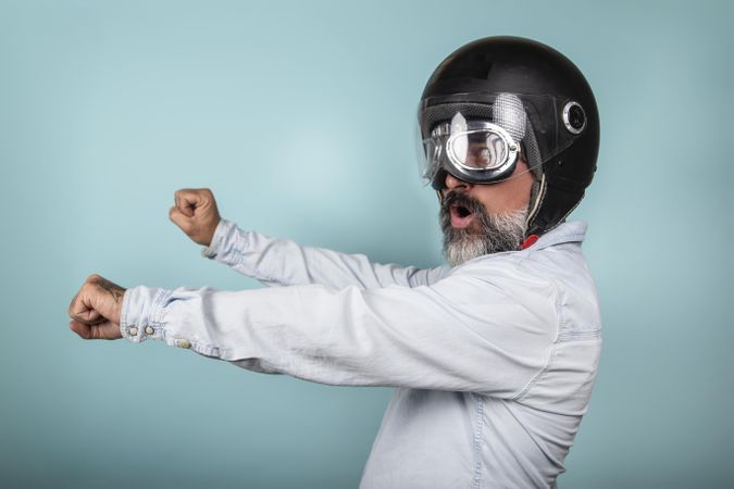 Side view of man with helmet and glasses pretending to ride a motorcycle in studio