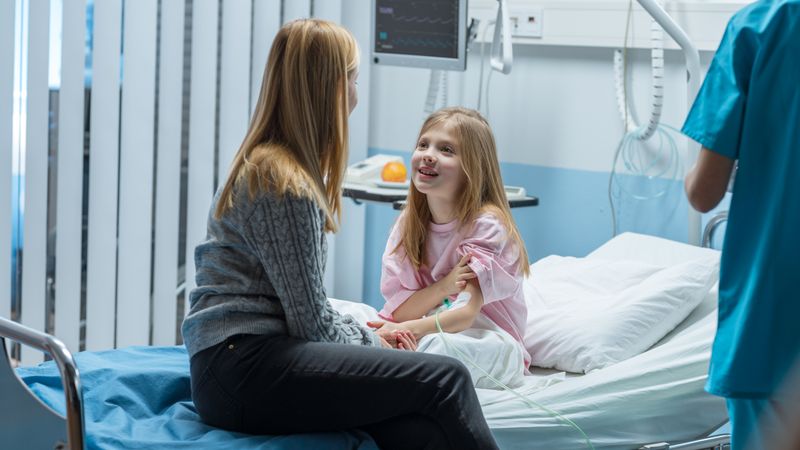 Healed Little Girl Sits on a Hospital Bed and Chats with Her Mother