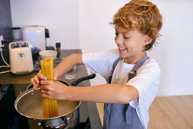 Smiling boy cooking raw spaghetti in pot on stove