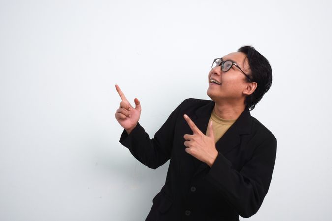 Joyful Asian businessman with suit and casual shirt pointing up and left