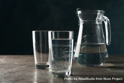 Two glasses of water in dark room on marble table with pitcher 56qML0