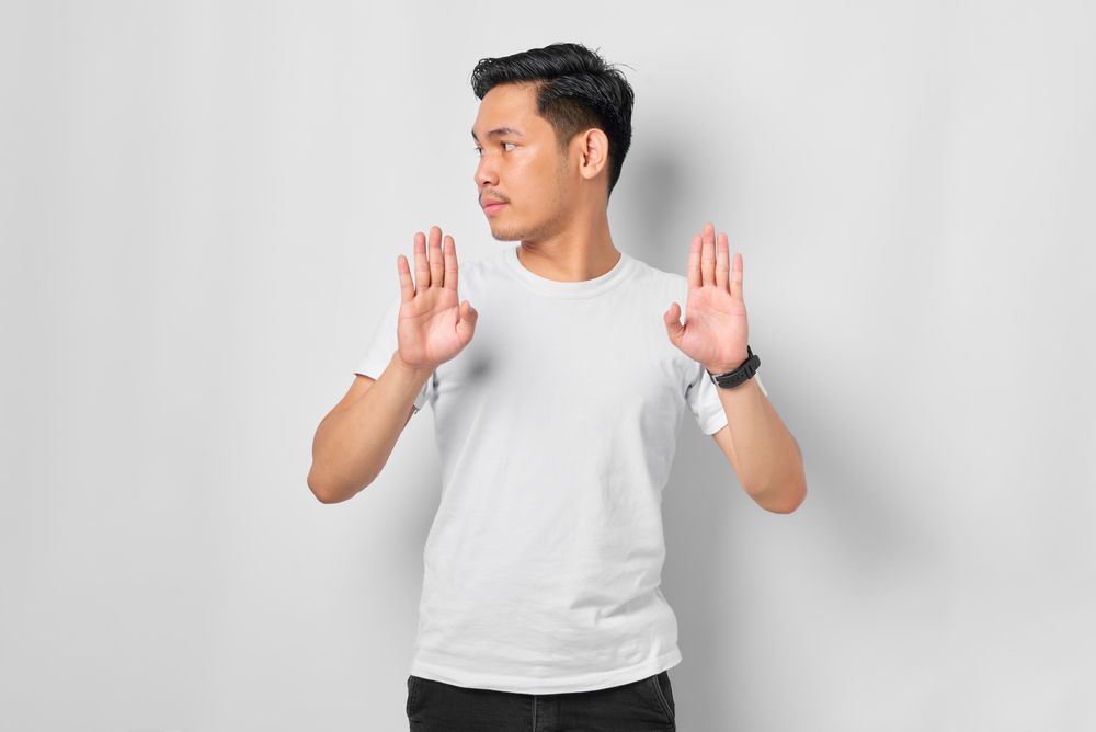 Asian male in grey studio gesturing “no” with both hands facing forward