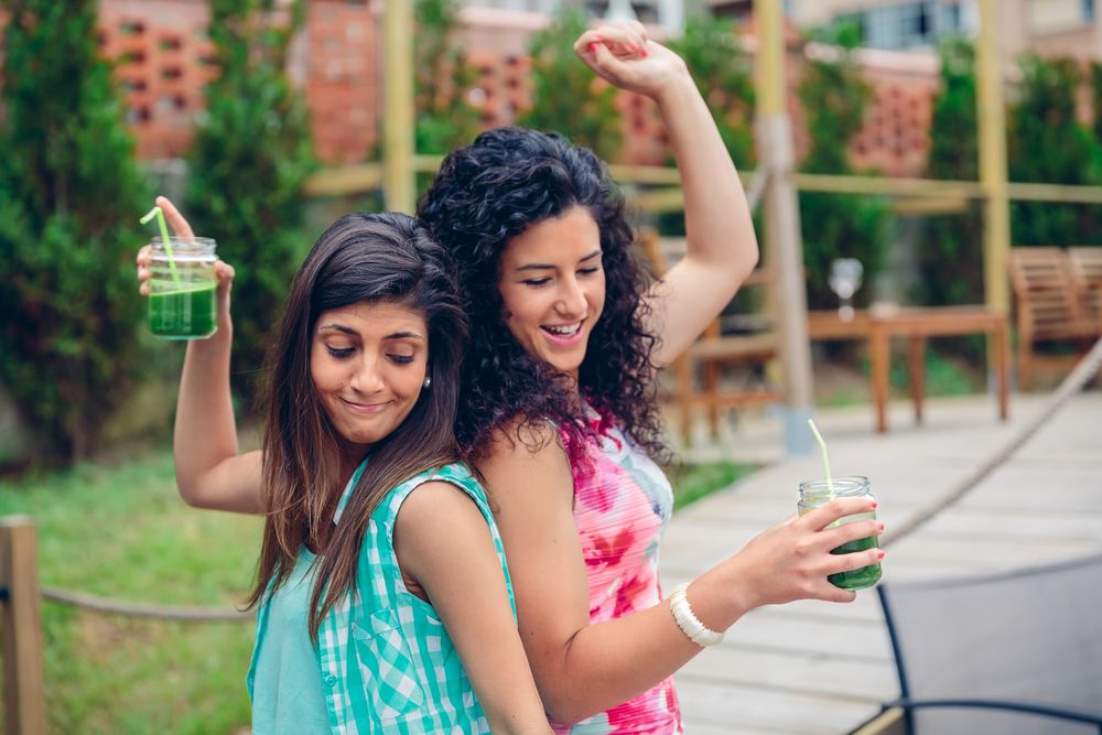 Two female friends dancing outside with cocktails