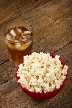 Bowl with salted popcorn and soda on the table.