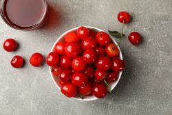 Bowl with red cherry and glass of juice on gray table, top view