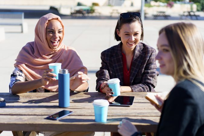 Laughing women sipping coffee on park picnic table