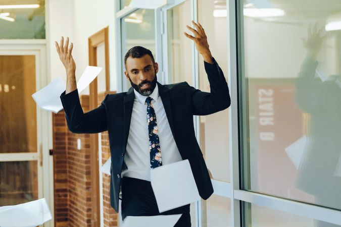 Annoyed businessman in suit and tie throwing papers in the air in frustration in office