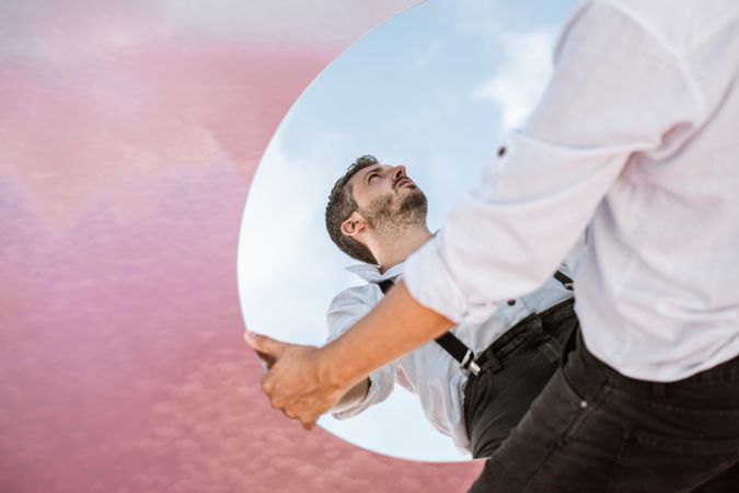 Stylish man holding mirror with reflection