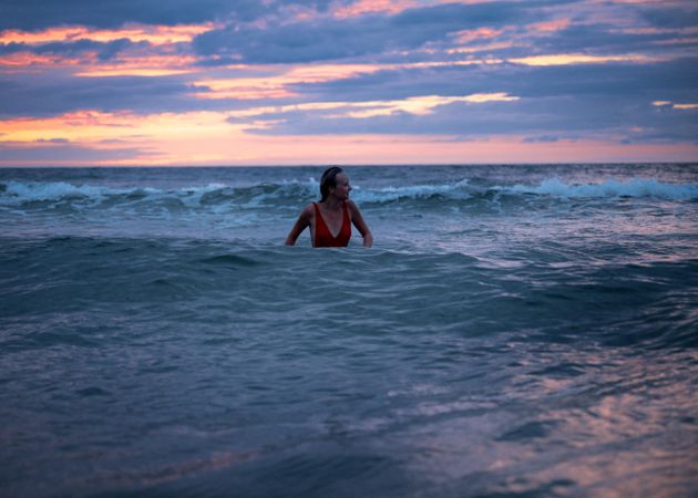Woman in red swimsuit wading in sea waves at sunset