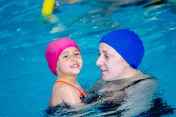 Cheerful girl swimming in pool with mother