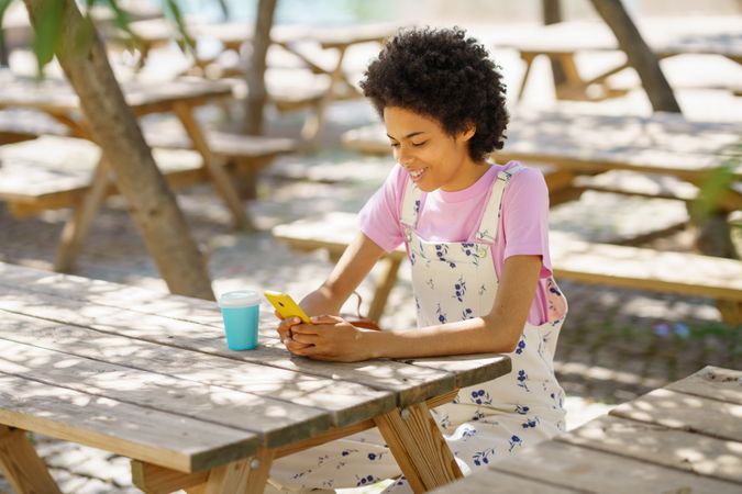 Happy woman sitting on park table texting