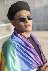 Gay man with make up on under LGBT rainbow flag while looking at camera. Concept of Pride. Pride month.