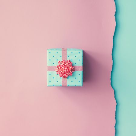 Close up shot of small gift wrapped with pink ribbon on pink blue background