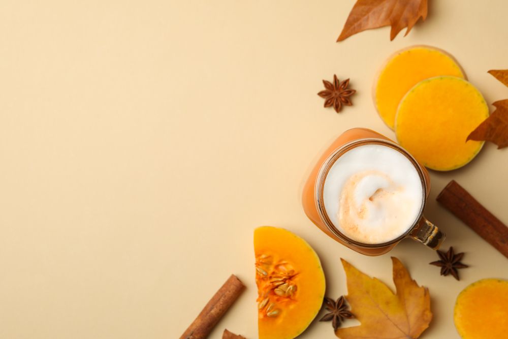Composition with pumpkin latte, pumpkin, leaves and cinnamon on beige background