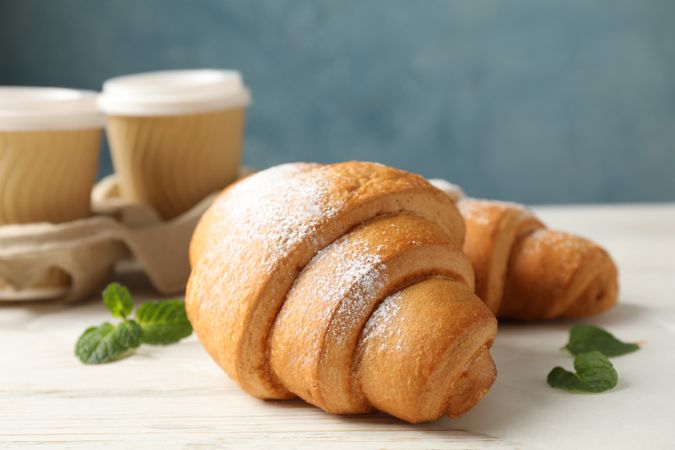 Two tasty croissants and cups of coffee in blue room