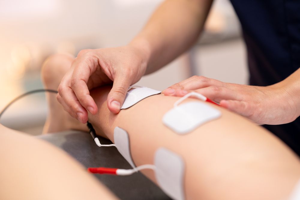 Physiotherapist placing electro pads for therapy on calf muscle of patient