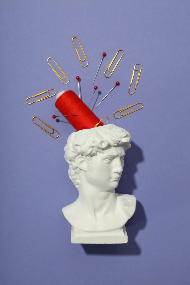Vertical composition of pins and red spool in bust on purple background