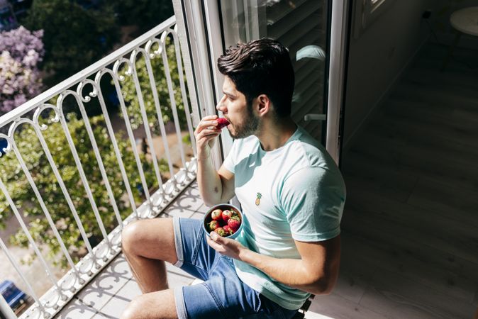 Young happy sexy male eating strawberry near terrace