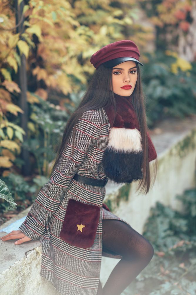 Female in warm clothes leaning on wall with orange leaves