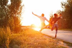 Back of girlfriend and boyfriend skipping on road at sunset