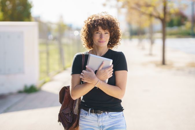 A Confident Young Woman Appears Holding a Laptop While Positioned in an Urban Setting