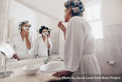 Two women with curling rollers to hair applying cream on face at home in the bathroom 47MMk0