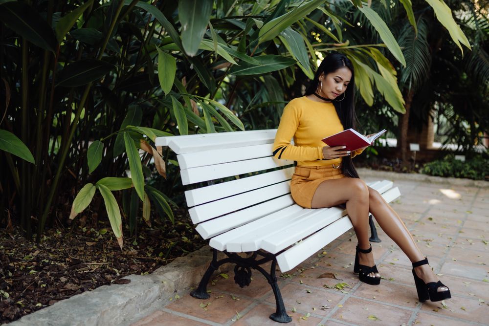 Graceful long haired Asian woman reading book on bench in park