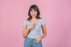 A woman pointing to a pink breast cancer awareness ribbon on her t-shirt.