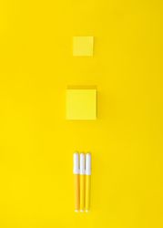 Three pens and post it notes on yellow background
