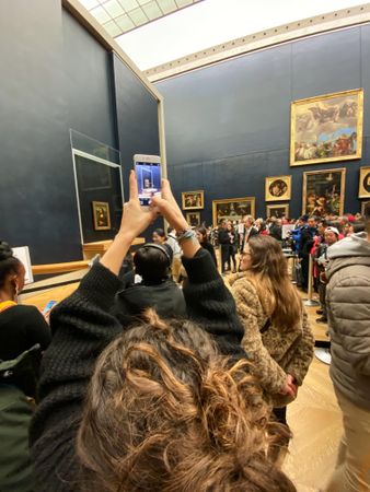 Back view of woman taking a photo using her cellphone at an art gallery in Paris, France