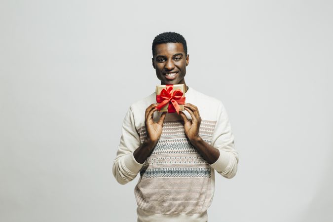 Smiling Black man holding gold box with red bow below his face