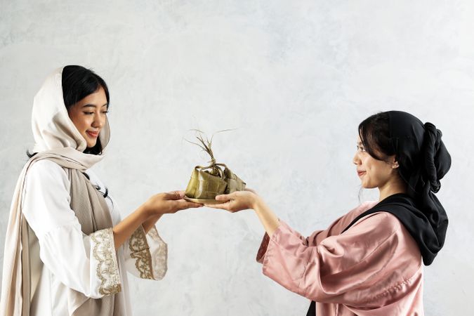 Two Female Sharing Ketupat for Eid Mubarak