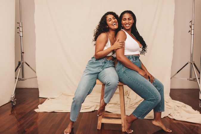 Two happy female friends having fun while sitting together in denim jeans and bras