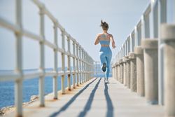 Unrecognizable jogger running on bridge above ocean during worko