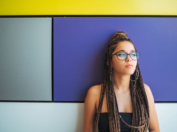 Charming teenage girl with braids in sunglasses nearby colorful wall