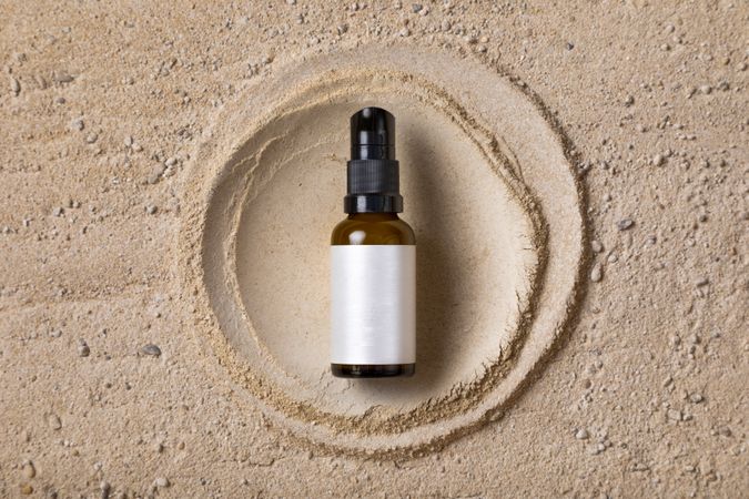 Mockup of an amber glass bottle of a cosmetic product on a sand texture and a circle