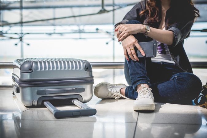 Female traveler sitting on bright airplane floor next to suitcase