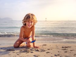 Smiling boy playing with toy shovel on sandy beach