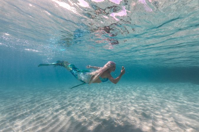 Blond fairytale female mermaid exploring underwater
