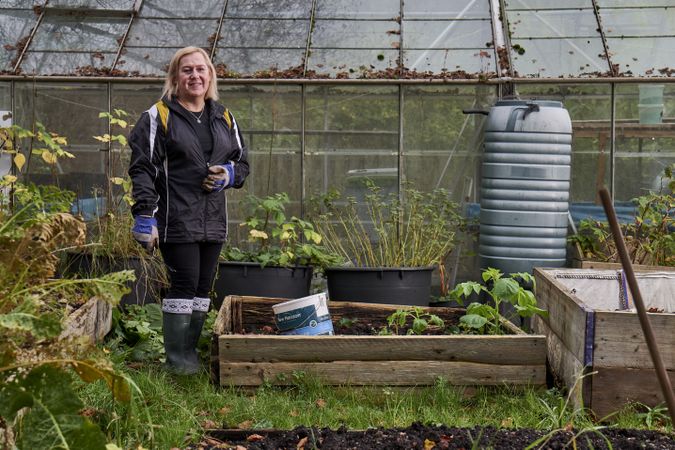 Smiling woman with plant box outside greenhouse