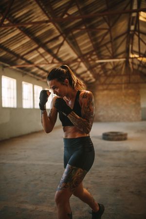 Fit young female practicing shadowboxing in old empty warehouse
