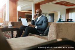 Male executive waiting in hotel lobby using cell phone and working on laptop 5nOVQ4