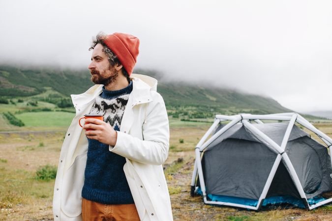 Man waking up from tent with ceramic mug